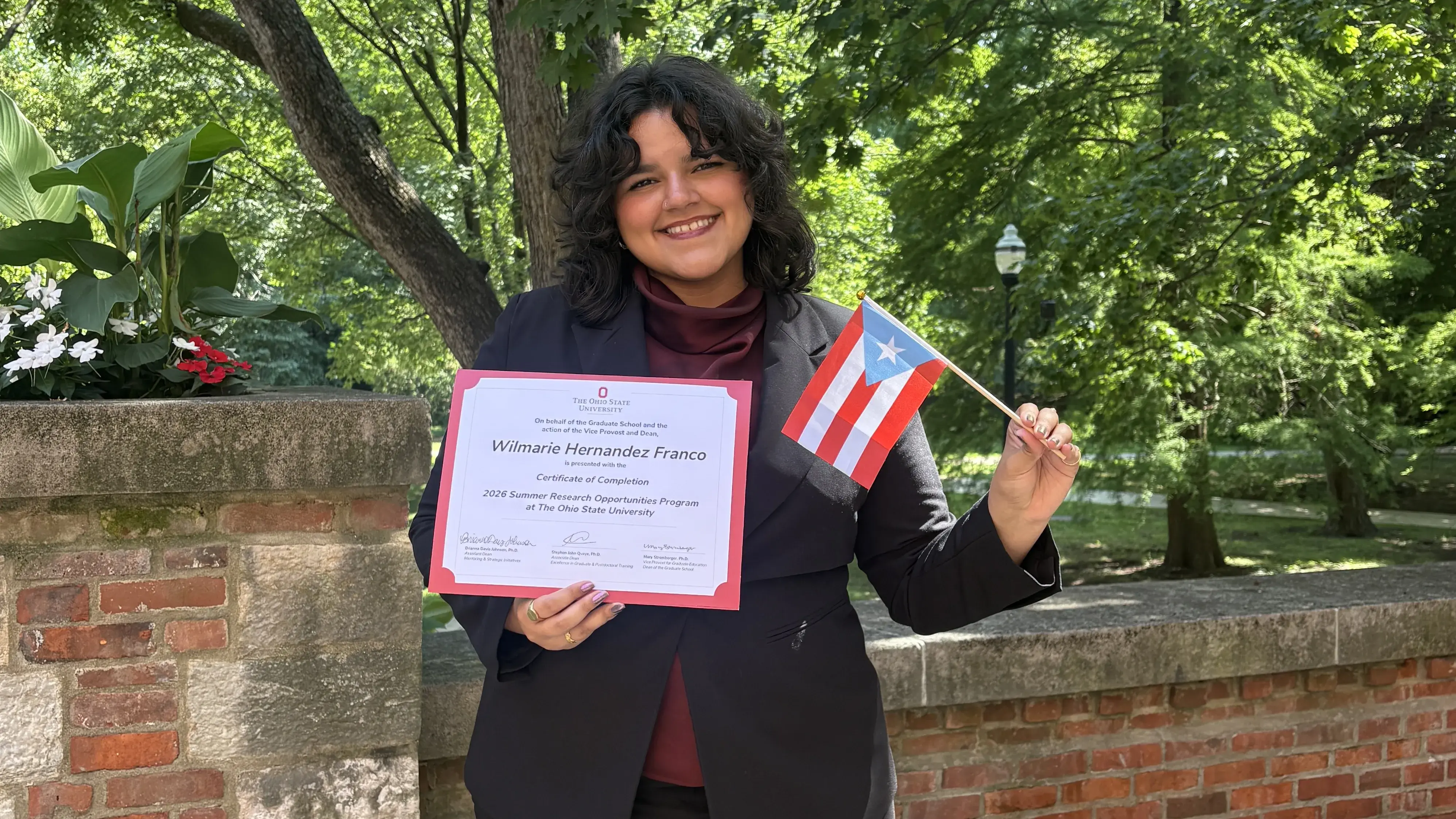 Wilmarie posing with her certificate of completion in front of a tree