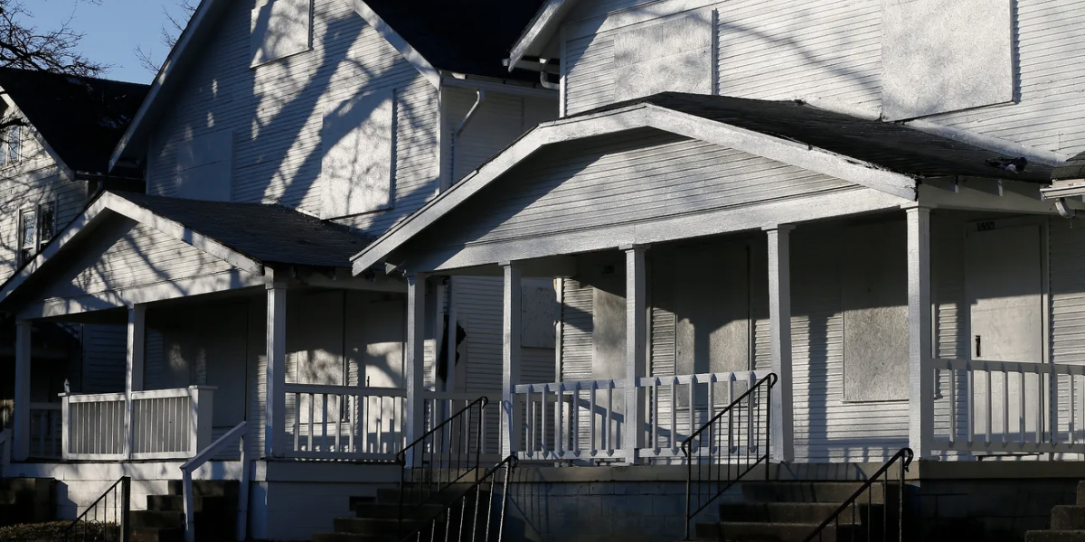 Screenshot of condemned white houses with boards over the front windows.